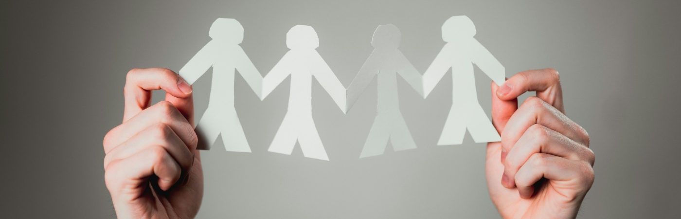 Hands holding up paper silhouettes of people.