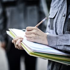 Person standing, holding a large folder and writing notes