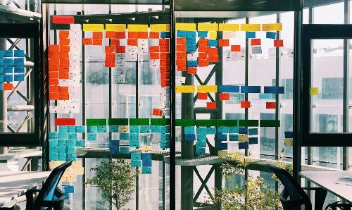 A glass board covered in post it notes with ideas on.